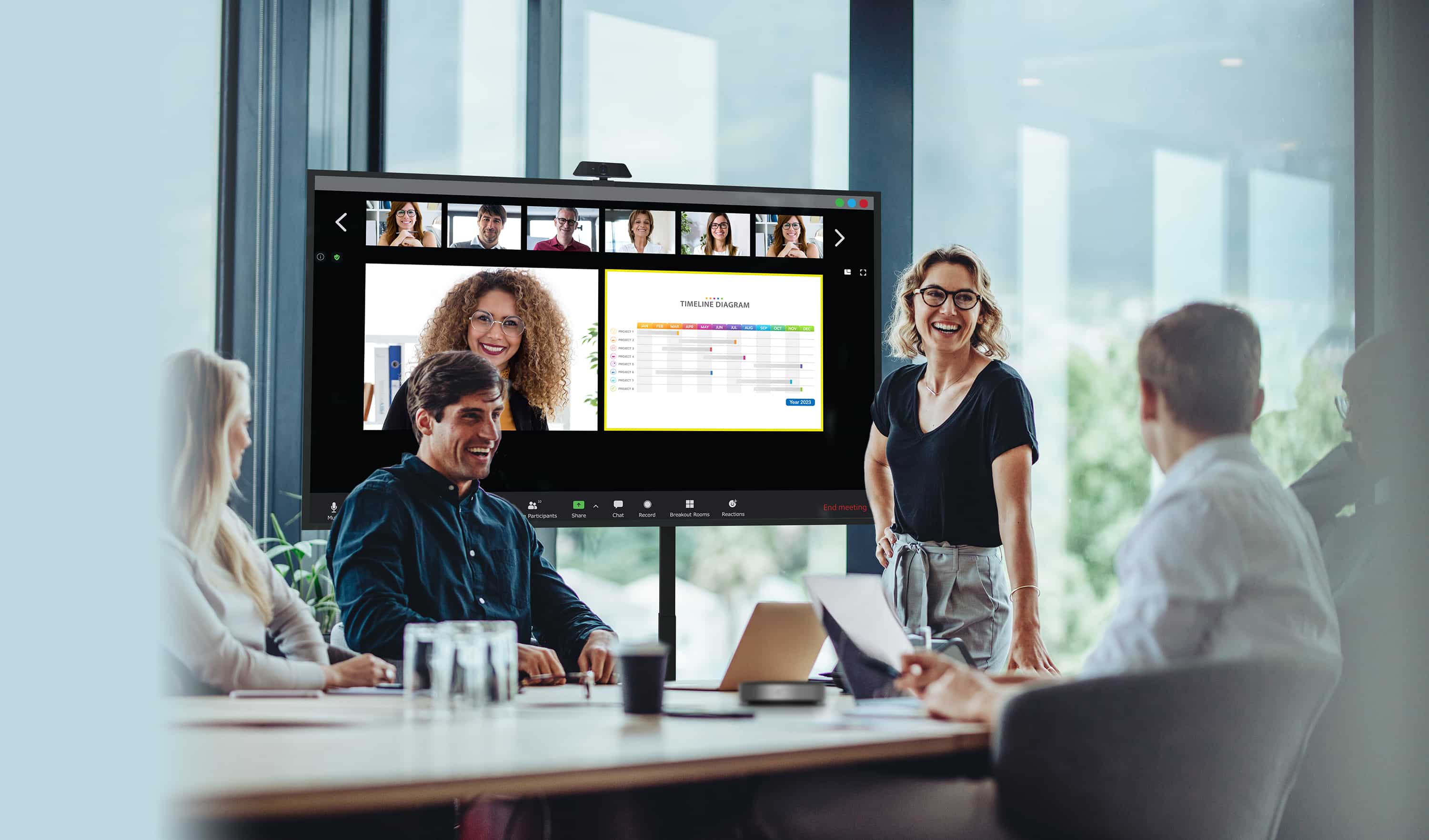 Uomini d'affari che conducono una riunione con parte del personale fisicamente presente che guarda un display Optoma N-Series mentre i loro colleghi remoti vengono mostrati sullo schermo accanto al contenuto che stanno condividendo.